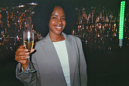 Young african american woman smiling and celebrating at a party, holding a glass of champagne with a...