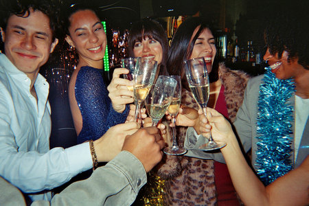 Group of diverse friends celebrating and making a toast with champagne glasses at a lively party or nightlife event, enjoying the festive atmosphere togetherの写真素材