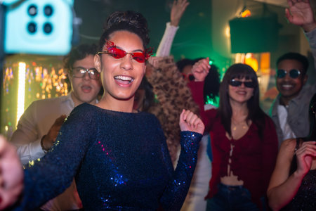 Diverse friends dancing and smiling in a vibrant club, moving to music under colorful lights,...