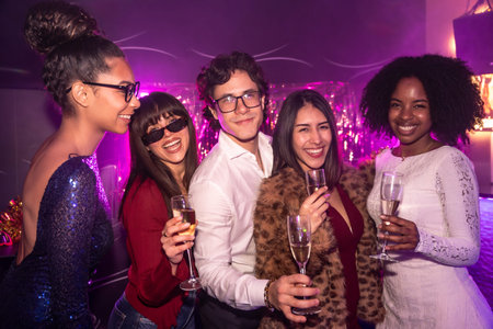 Diverse group of smiling friends celebrating together during a festive event, holding champagne...