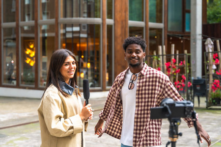 Journalist holding a microphone interviewing a young man on a city street, documenting the conversation with a camera on a tripod for a live broadcast or social media contentの写真素材