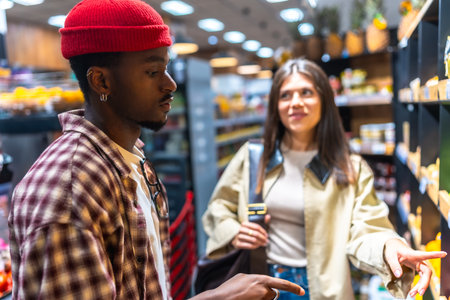 Diverse young couple selecting fresh produce in a modern supermarket aisle, comparing options and enjoying a healthy daily shopping routine together with smiles and casual conversationの写真素材
