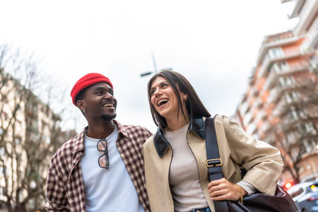 Young diverse couple walking and laughing on a city street, sharing a joyful, candid moment of connection, friendship and relaxed, stylish urban togethernessの写真素材