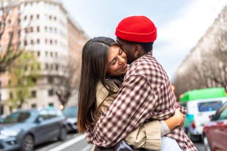 Young diverse couple embracing on an urban street, expressing love and affection, with a multi ethnic man kissing the smiling woman's cheek while surrounded by city buildings and carsの写真素材