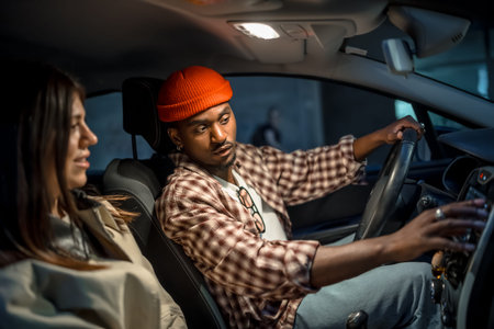 Young couple on a nighttime road trip, man driving while woman navigates and they chat over the...
