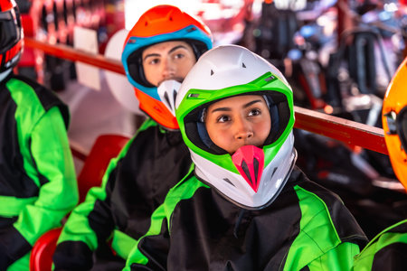 Young man and woman in racing suits and helmets sit in a go kart at the starting line, focused and ready for a fast, adrenaline filled race on a bright outdoor trackの写真素材