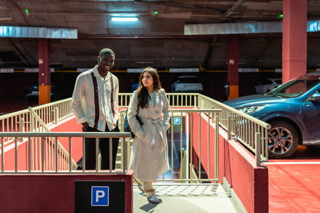 Diverse interracial couple walking up concrete stairs in an urban parking garage, smiling and...