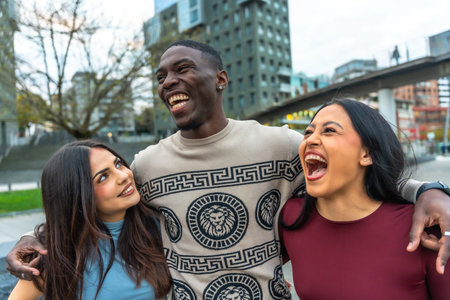 Three multiethnic friends laughing and embracing on a city street, sharing joyful, candid moments of connection and togetherness in an urban lifestyle sceneの写真素材