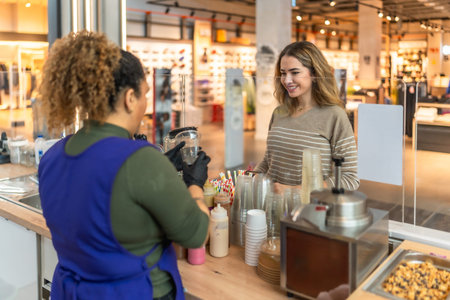 Smiling woman making a purchase at a juice bar counter, interacting with a friendly female employee...