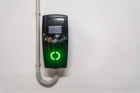Electric vehicle wallbox charger mounted on a white wall in valencia, spain, glowing bright green to...