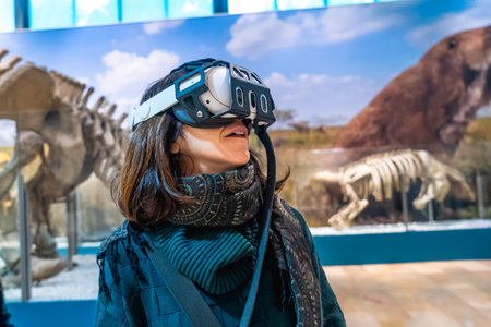 Woman experiencing virtual reality with a headset on, exploring ancient animals and paleontology in a modern museum exhibition, blending technology with educationの写真素材