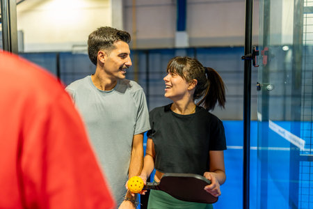 Two smiling adult players holding a paddle and ball, sharing a moment during a friendly pickleball match, representing an active lifestyle and leisure activityの写真素材