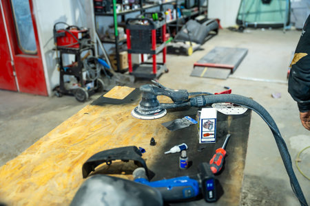 Orbital sander, hand tools, and car parts sitting on a wooden workbench inside a busy automotive...