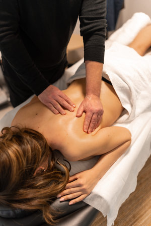 Professional masseur applying pressure and circular motions on a woman's bare back, providing a...