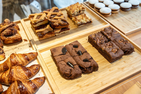 Various baked goods including croissants, tarts, and brownies arranged on wooden trays, showcasing a...