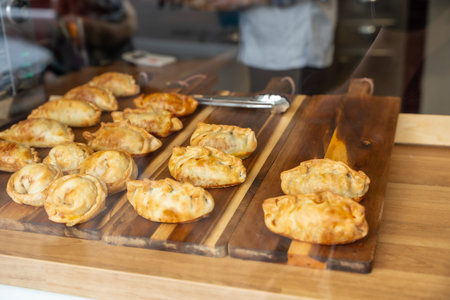 Golden brown empanadas featuring various shapes and fillings, arranged enticingly on dark wooden...