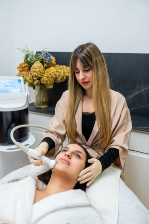 Young woman relaxing while a beautician performs a facial aesthetic treatment using advanced...