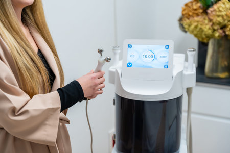 Woman holding a modern microneedling device, preparing for a facial skin treatment at a professional...