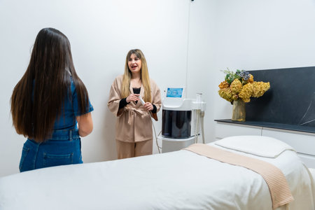 Professional aesthetician explaining a skincare treatment procedure to a female client in a bright,...