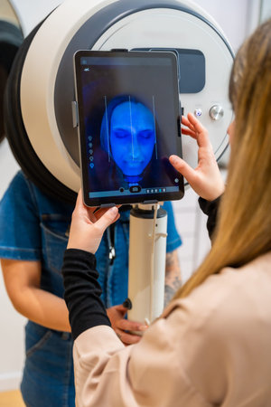 Professional examines a client's face on a tablet displaying advanced facial scanner imaging for...