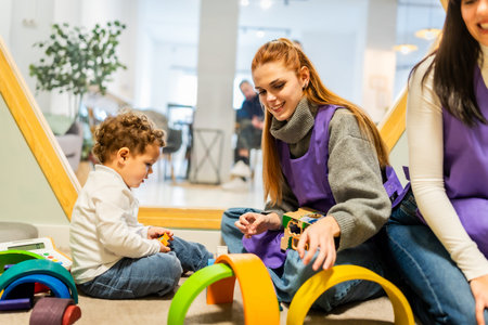 Happy teacher engaging with a small child on the floor, building and learning with colorful wooden blocks and educational toys in a bright indoor daycare setting