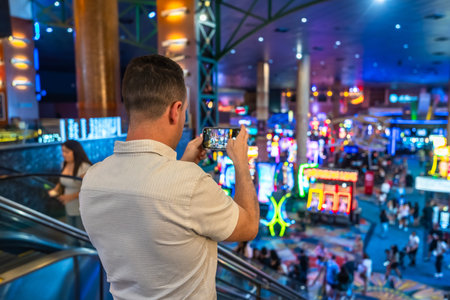 Tourist on an escalator using a smartphone to capture the vibrant, colorful lights and exciting atmosphere of a busy casino floor in las vegas, nevada