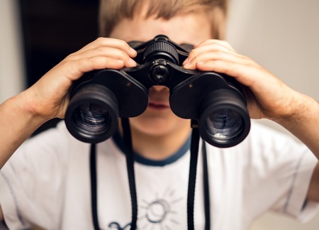 Boy looks in binoculars on the background of a white wall.の写真素材