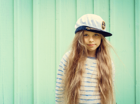 Cute little girl stands near a turquoise wall in sailor hat and smiling Space for text. Negative space.の写真素材