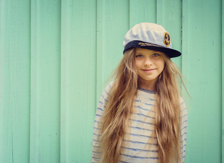Cute little girl stands near a turquoise wall in sailor hat and smiling Space for text. Negative space.の写真素材