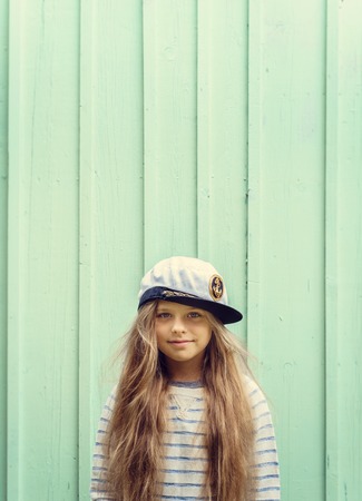 Cute little girl stands near a turquoise wall in sailor hat and smiling Space for text. Negative space.の写真素材