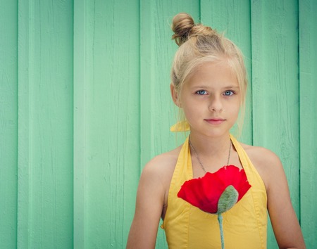 Cheerful young blond girl holding a red flower. Space for textの写真素材