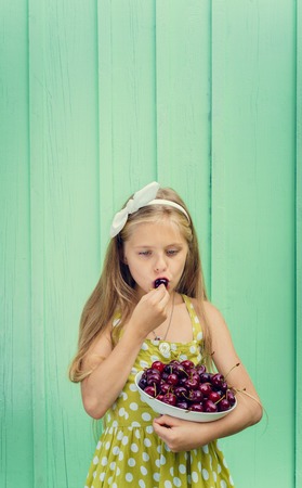 Beautiful blond girl on a background of turquoise wall holding a plate with cherry. Space for textの写真素材