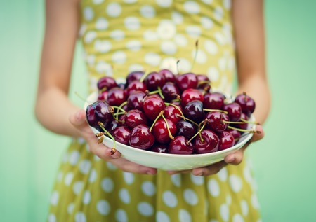 Girl on a background of turquoise wall holding a plate with cherry. Space for textの写真素材