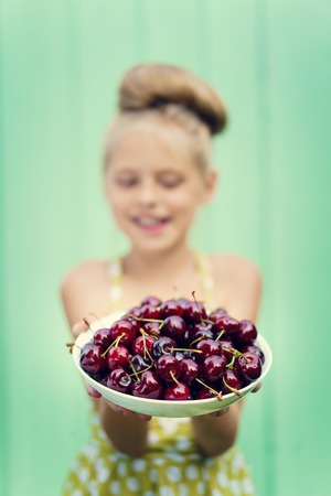 Girl on a background of turquoise wall holding a plate with cherry. Space for textの写真素材