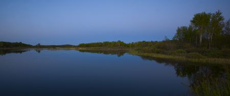 Night falls on a still blue lake and a green shore at Island lake in the north woods of minnesotaの写真素材