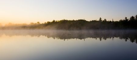 Sunrise burns away the morning mist at Boulder Lake in Northern Minnesotaの写真素材