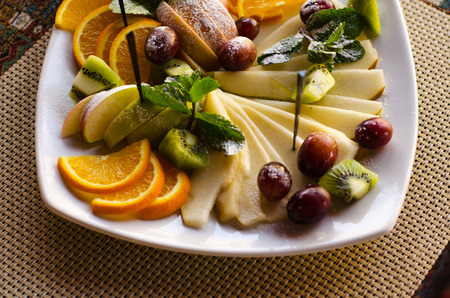Fruit. Apples, pears, kiwi, oranges, plums, decorated with mint on a white plate.の写真素材