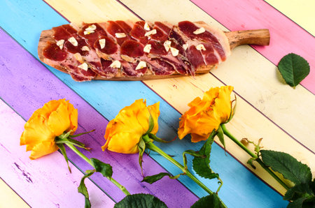 Cutting board  jamon and garlic on a colorful background. Nearby are beautiful flowers.