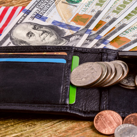 One hundred dollars banknote reach out out of a black old purse. And also part of the American flag....