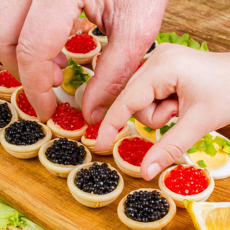 Human hands take tartlets with red and black caviar. Food background. Concept of luxury food....