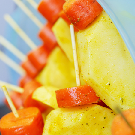 Raw carrots and potatoes, strung on a skewer for grilling. Prepared for a picnic. Selective focus. Concept of healthy, useful food. Square. Close-up.の写真素材