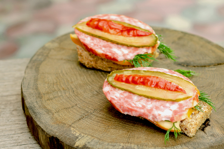 Two sandwiches with sausage, cheese and dill on a wooden stump. Selective focus. Close-up.の写真素材