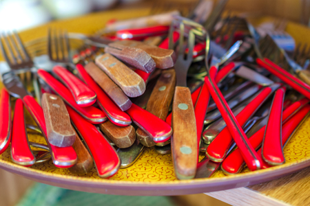 Pile of cutlery, forks and spoons, with red wooden handles lie on a tray. Artistic blur. Selective and soft focus. Close-up.の写真素材