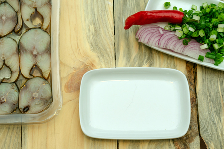 Preparation of a homemade snack from smoked mackerel. Smoked fish in box and  the dish with onions and red papper chili for decorating. Top view. Close-up.の写真素材