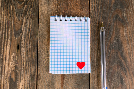 Notepad in cage, with small heart in lower corner and pen, lies on wooden table. The concept of...