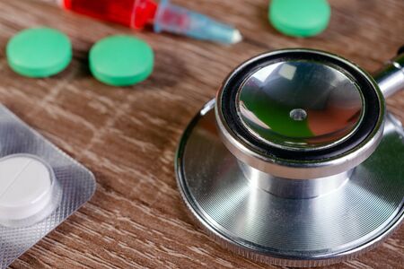 Stethoscope, pills, and syringe with red vaccine or injection on wooden table. Healthcare and medicine concept. Close-up.の写真素材