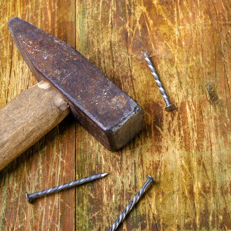 Old rusty hammer and three steel nails lie on a scratched wooden table. Copy space for text....