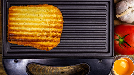 Grilled white toast bread with golden crust in stripes lies in open black sandwich maker, on wooden...