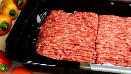 Raw minced meat in a plastic packing and colorful vegetables lies on the kitchen table. 16x9 format....