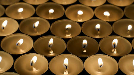 Many burning round small candles with reflections are burning in dark. Fire background. Selective focus. Close-up.の写真素材